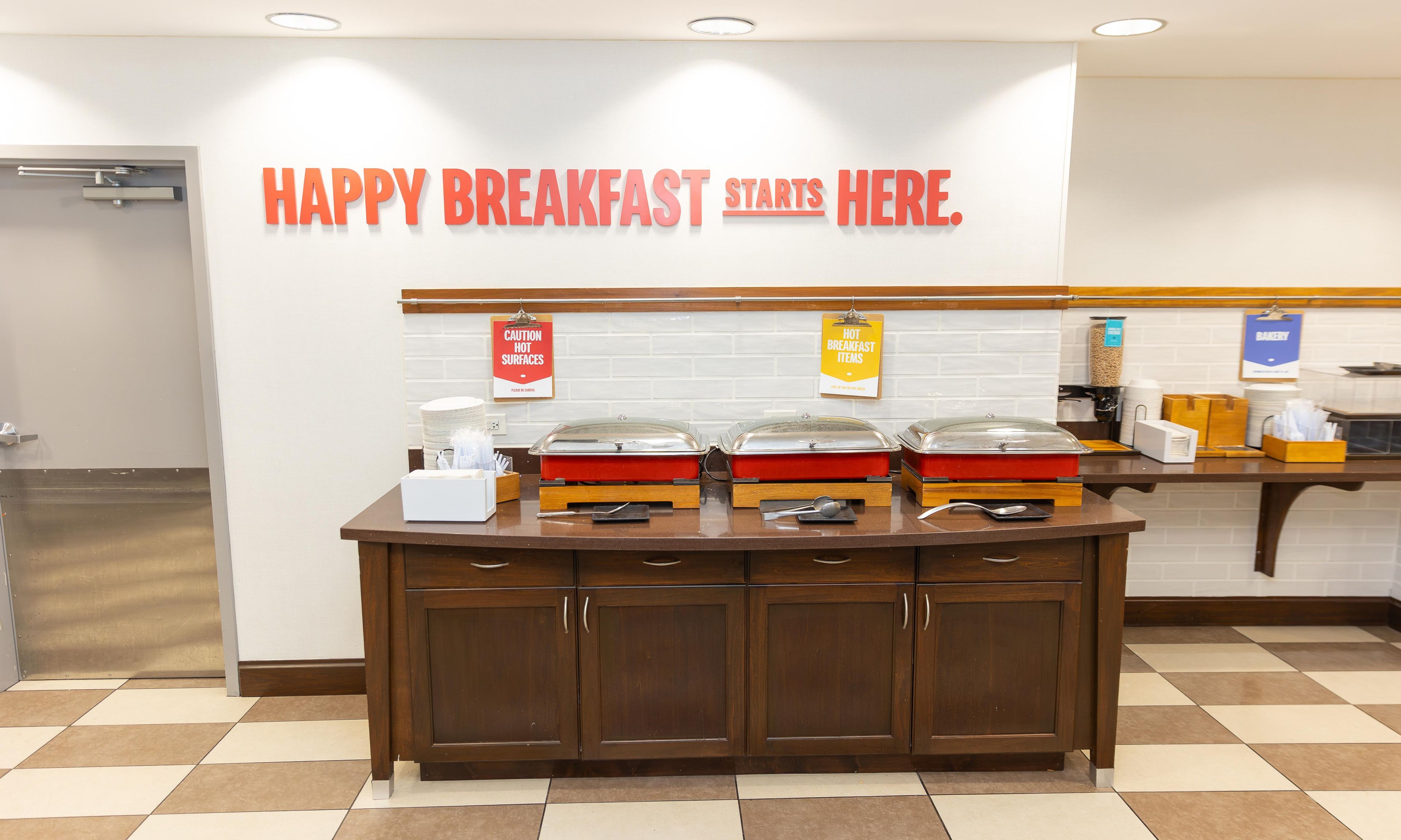 A breakfast buffet area with a sign that reads 'HAPPY BREAKFAST STARTS HERE.'