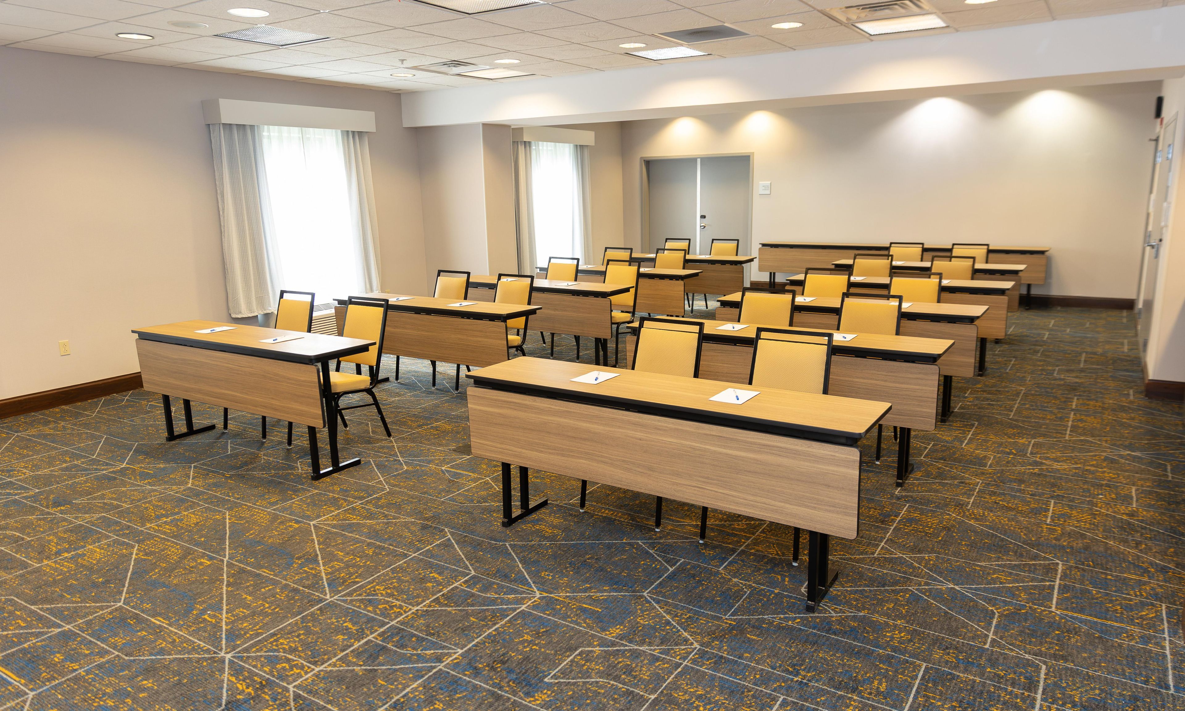 A conference room with multiple tables and chairs, a patterned carpet, and a plain wall with a door.