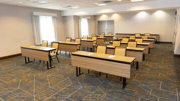 A conference room with multiple tables and chairs, a patterned carpet, and a plain wall with a door.