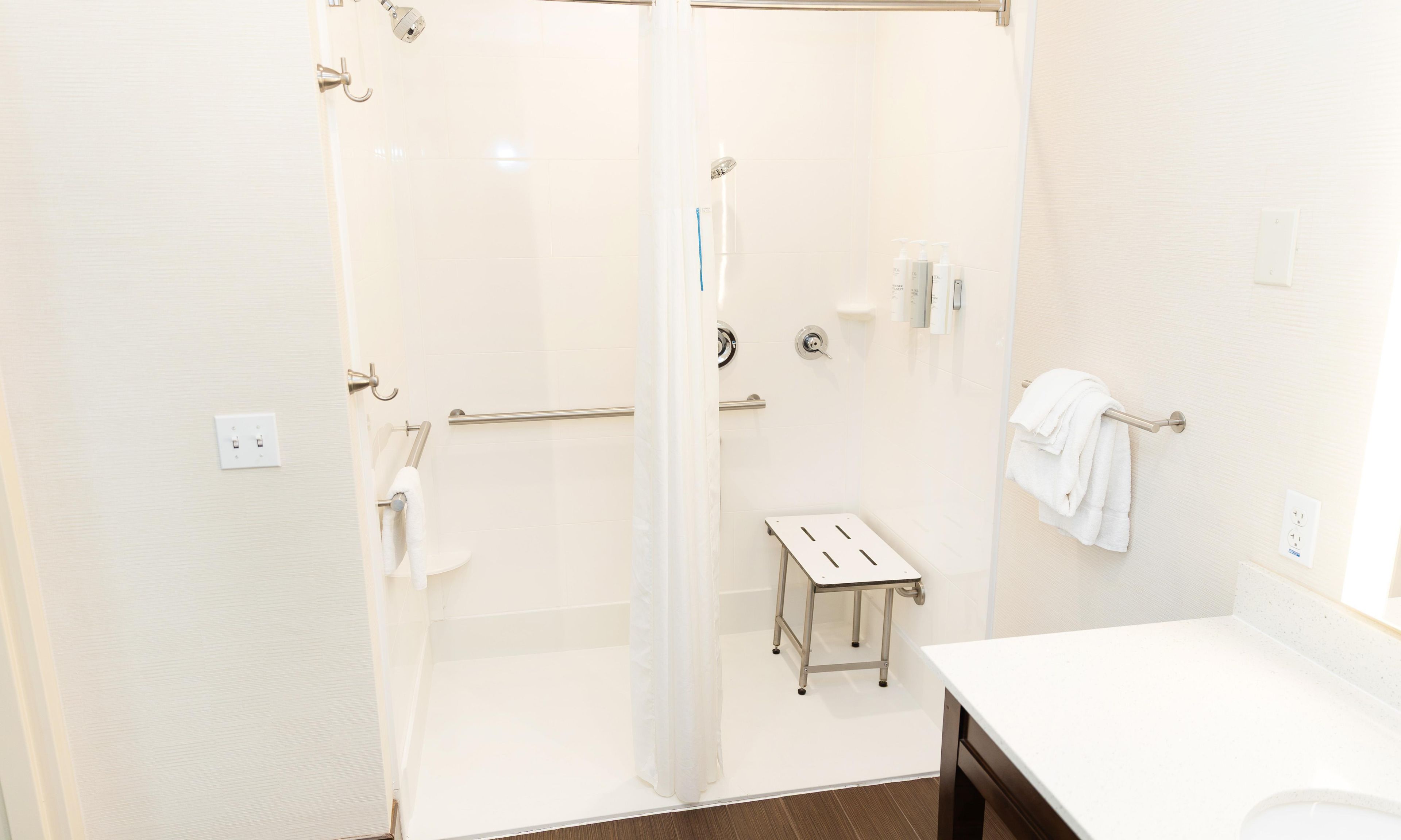 Een badkamer met een douchecabine van glas, een wit wastafeltje en een klein tafeltje.
