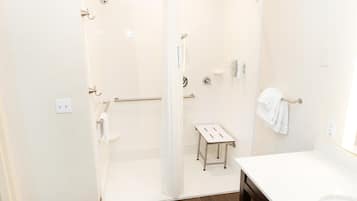 Een badkamer met een douchecabine van glas, een wit wastafeltje en een klein tafeltje.