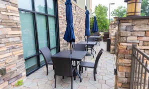 An outdoor patio with stone walls, tables, chairs, and blue umbrellas.