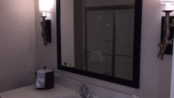 Un baño con un espejo grande, un lavamanos, un perchero para toallas y un dispensador de papel higiénico.
