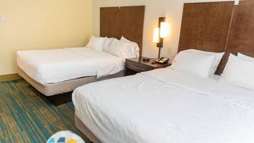 A hotel room with two beds, a nightstand with a phone, and a wall-mounted light.