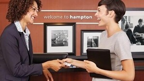 A reception desk with a sign that reads "welcome to Hampton" and framed pictures on the wall.