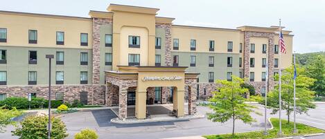 Un hotel Hampton Inn & Suites con fachada de piedra, varias ventanas y un estacionamiento.