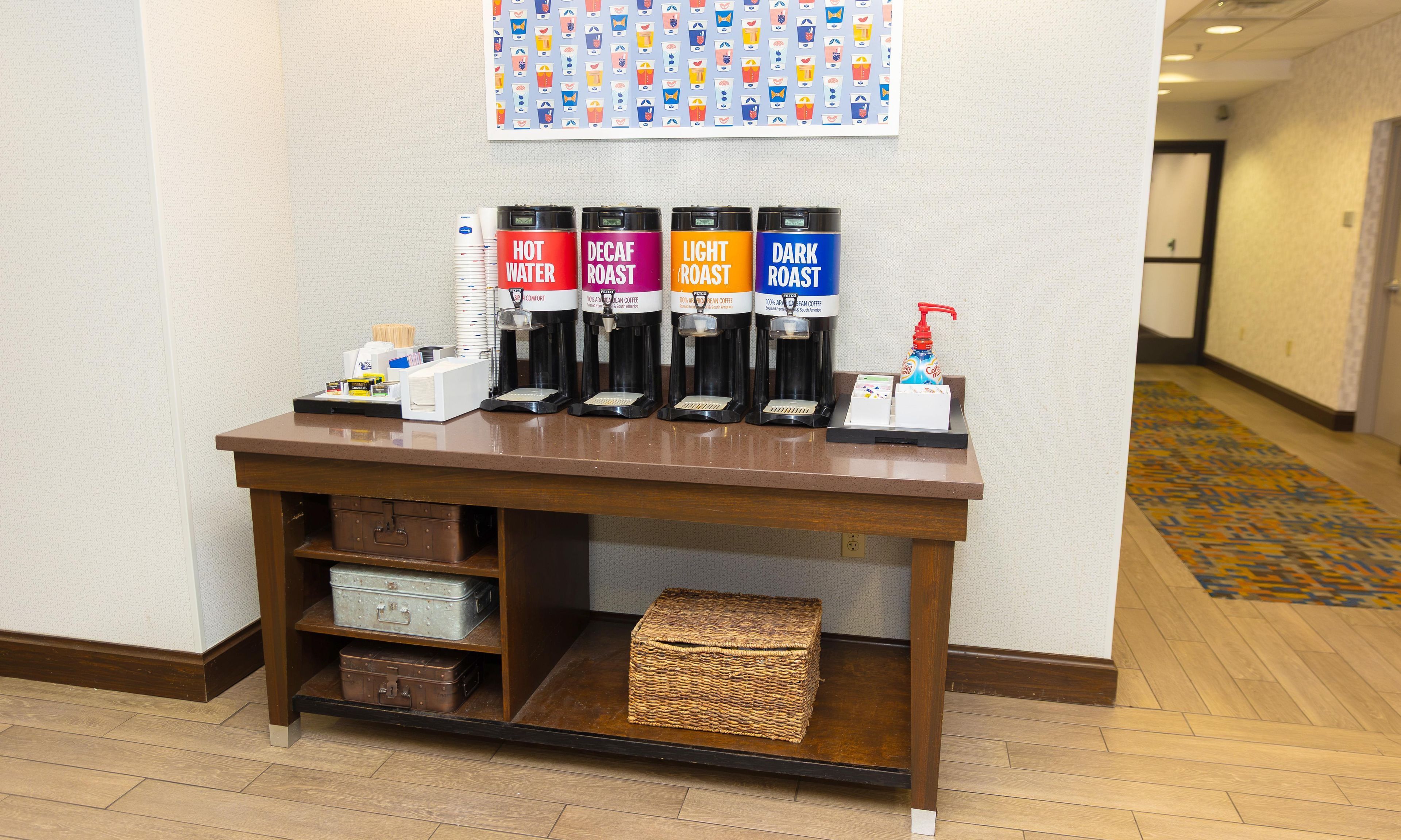 A coffee station with four coffee dispensers labeled hot water, decaf roast, light roast, and dark roast.