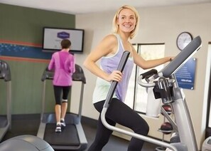 Un gimnasio con cintas de correr y una pantalla fijada en la pared.