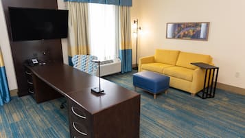 Una camera d'albergo con una scrivania, un divano, una TV, un quadro e una lampada.