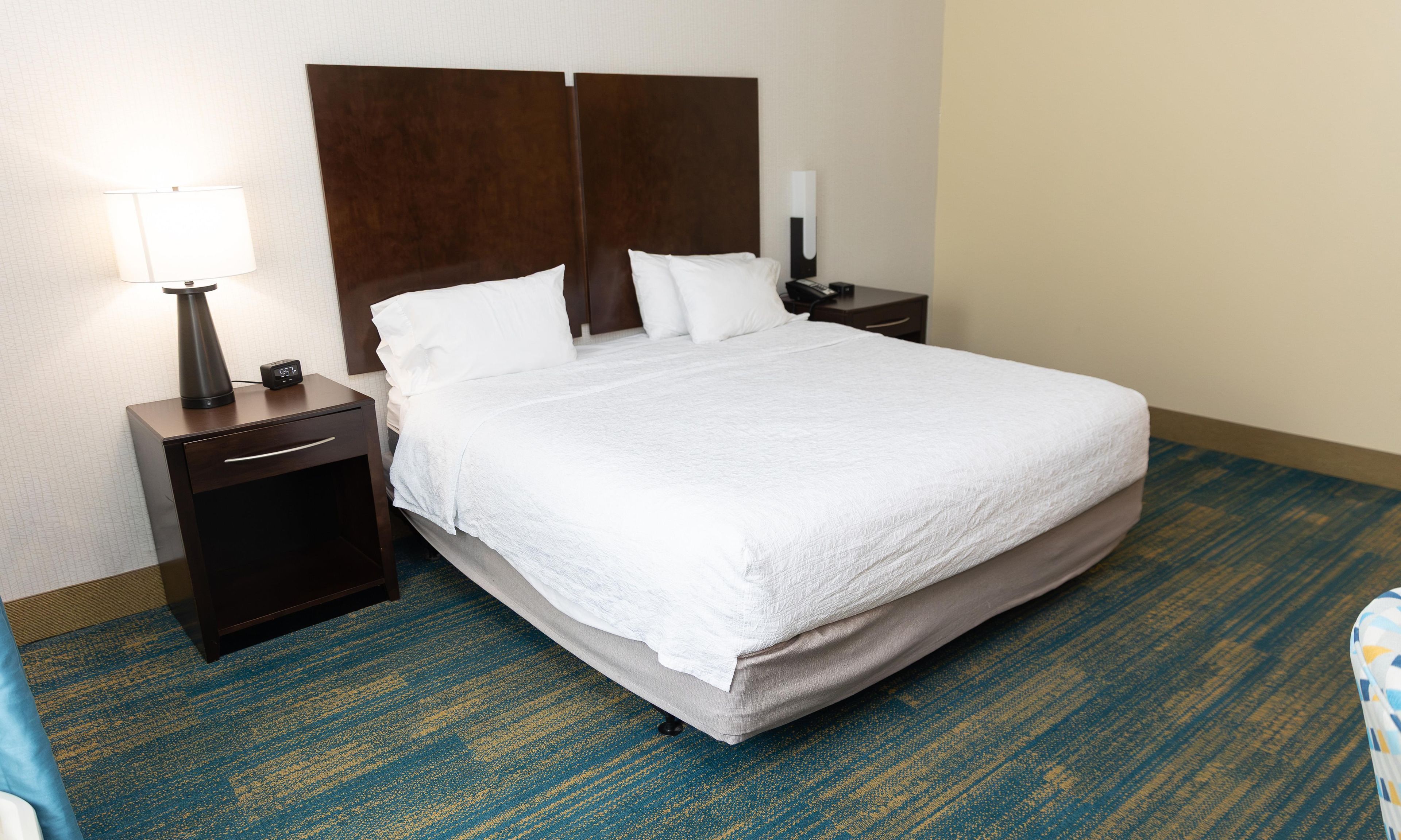 Habitación de hotel con una cama grande, una mesita de noche con lámpara y un teléfono en la pared.