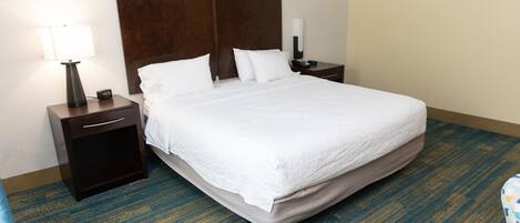 Habitación de hotel con una cama grande, una mesita de noche con lámpara y un teléfono en la pared.
