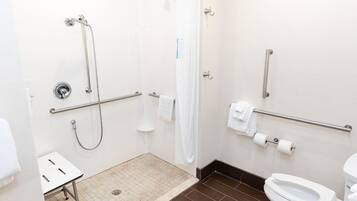Une salle de bain équipée d’une douche, de toilettes, de barres d’appui et d’un banc accessible aux personnes en fauteuil roulant.