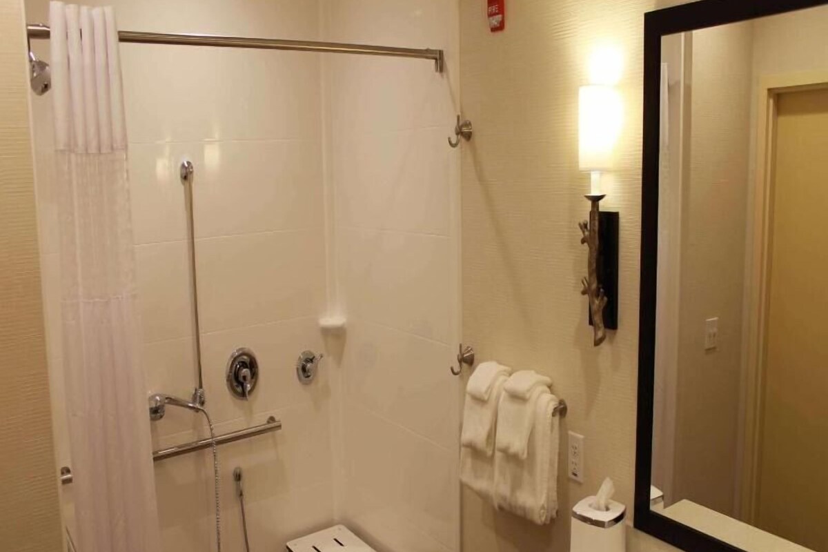 Un bany amb dutxa, un lavabo, un mirall i un suport per a tovallons.