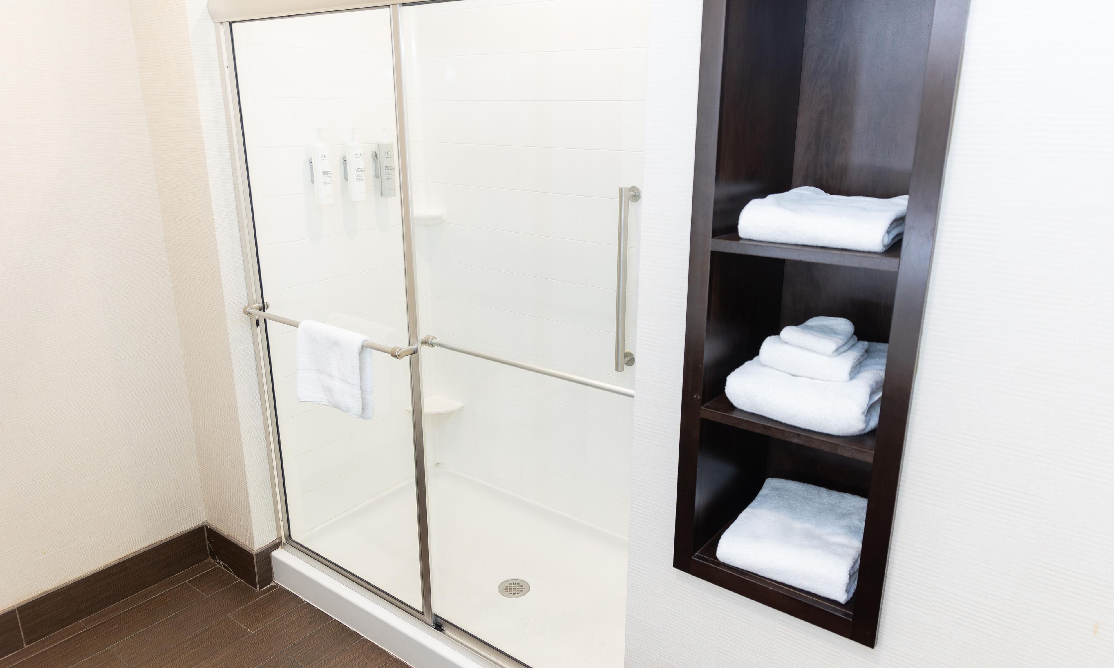 A bathroom with a glass shower enclosure, a towel rack, and a shelf with folded towels.