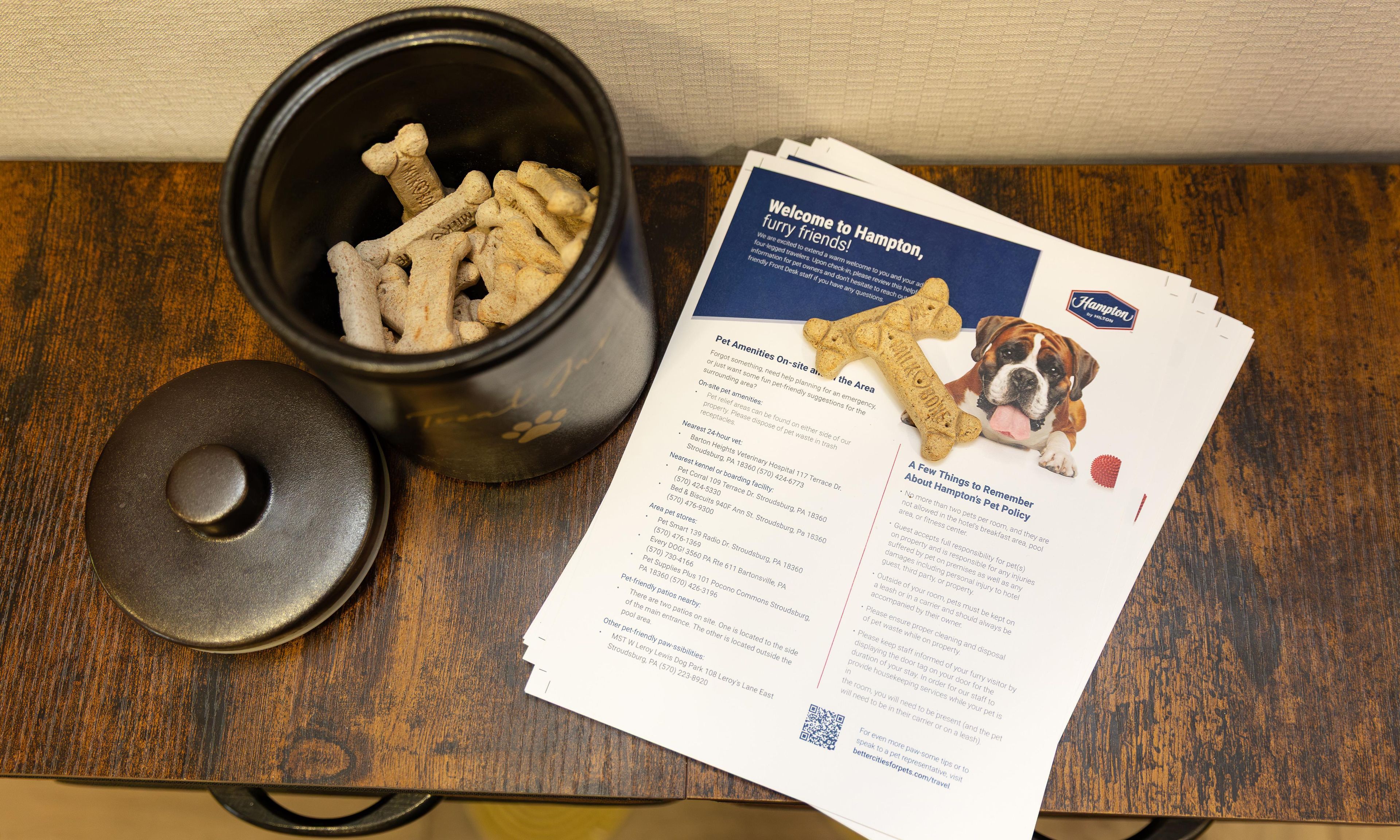 Een zwarte container met hondenkoekjes, een brochure met de titel 'Welcome to Hampton' en een houten tafel.