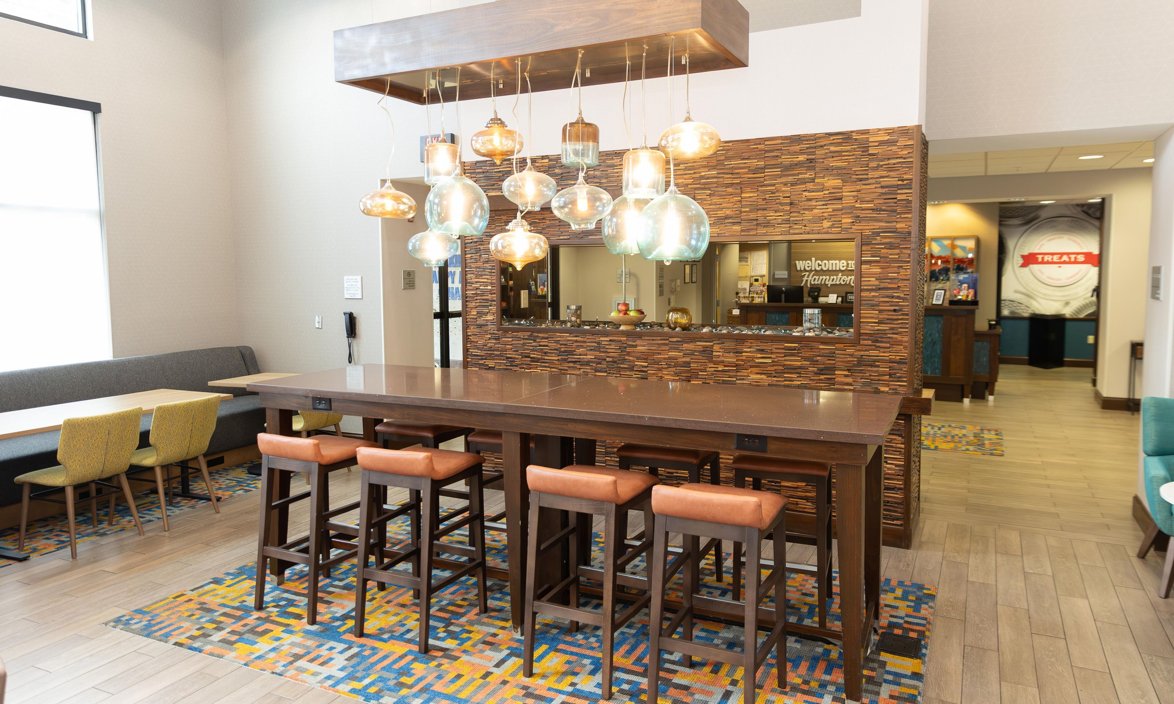 Un espace bar avec un comptoir en bois, de nombreux tabourets, un tapis à motifs et un miroir au-dessus du comptoir.