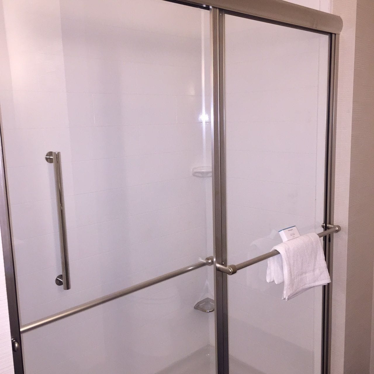 A glass-enclosed shower stall with a metal frame, a towel rack, and a glass shelf.
