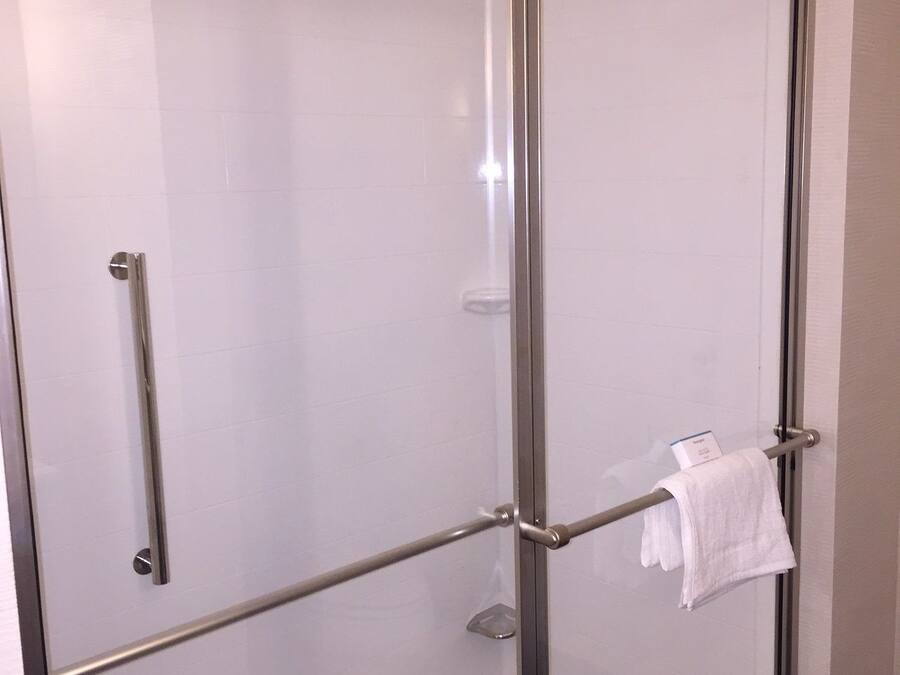 A glass-enclosed shower stall with a metal frame, a towel rack, and a glass shelf.