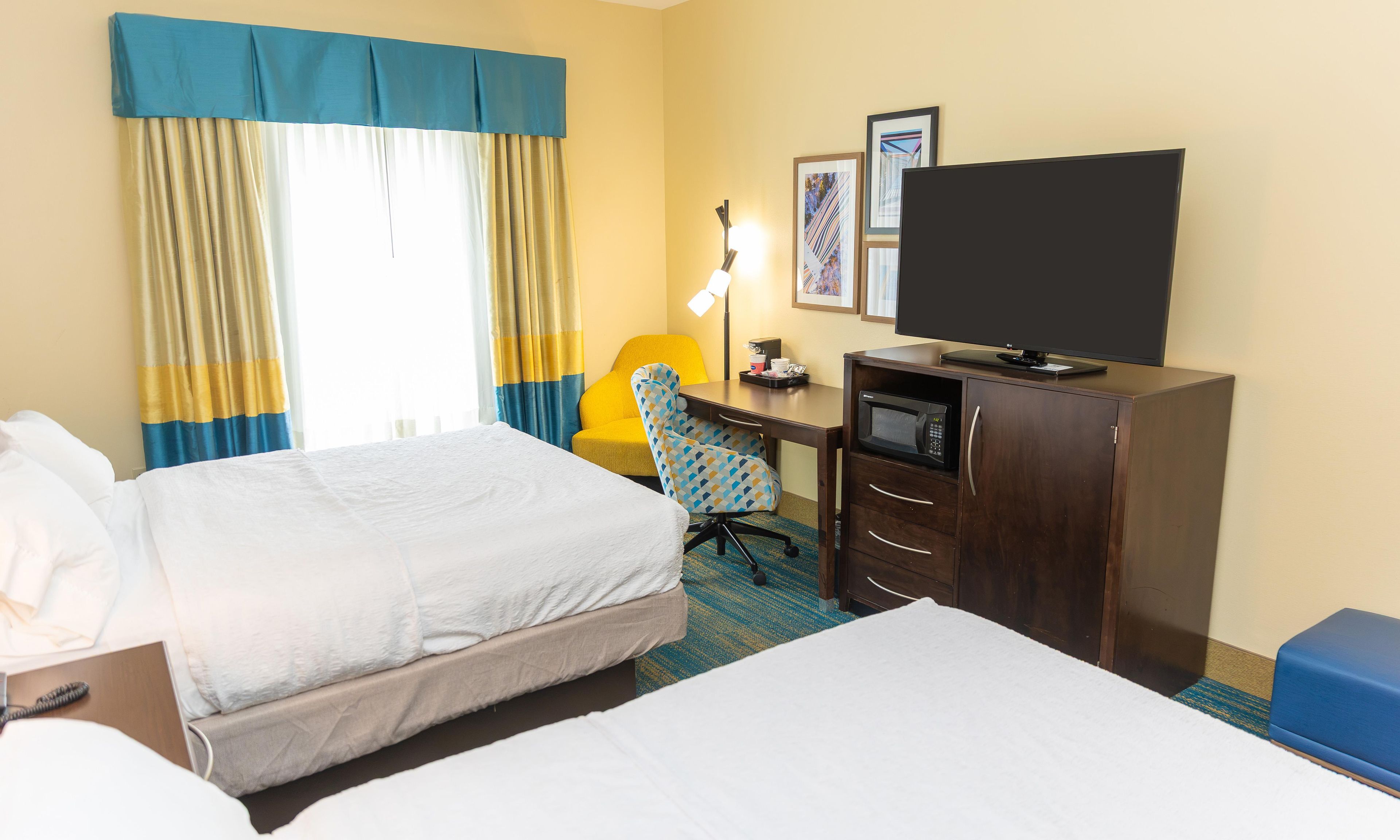 A hotel room with two beds, a desk with a microwave, a chair, and a television.