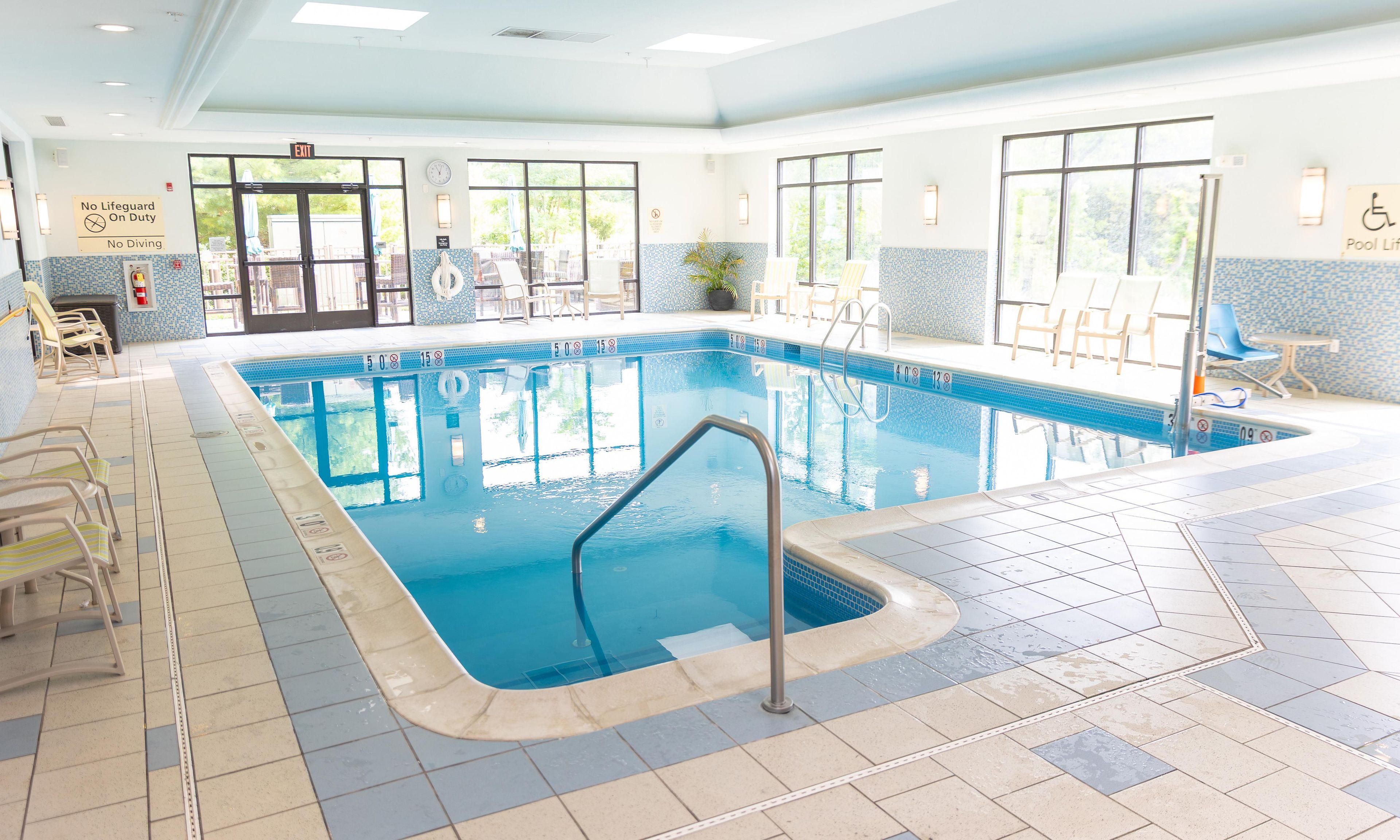 An indoor swimming pool with clear water, tiled floor, and multiple lounge chairs.
