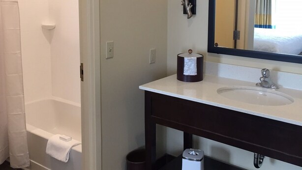 A bathroom with a bathtub, a sink, a mirror, and a towel rack.