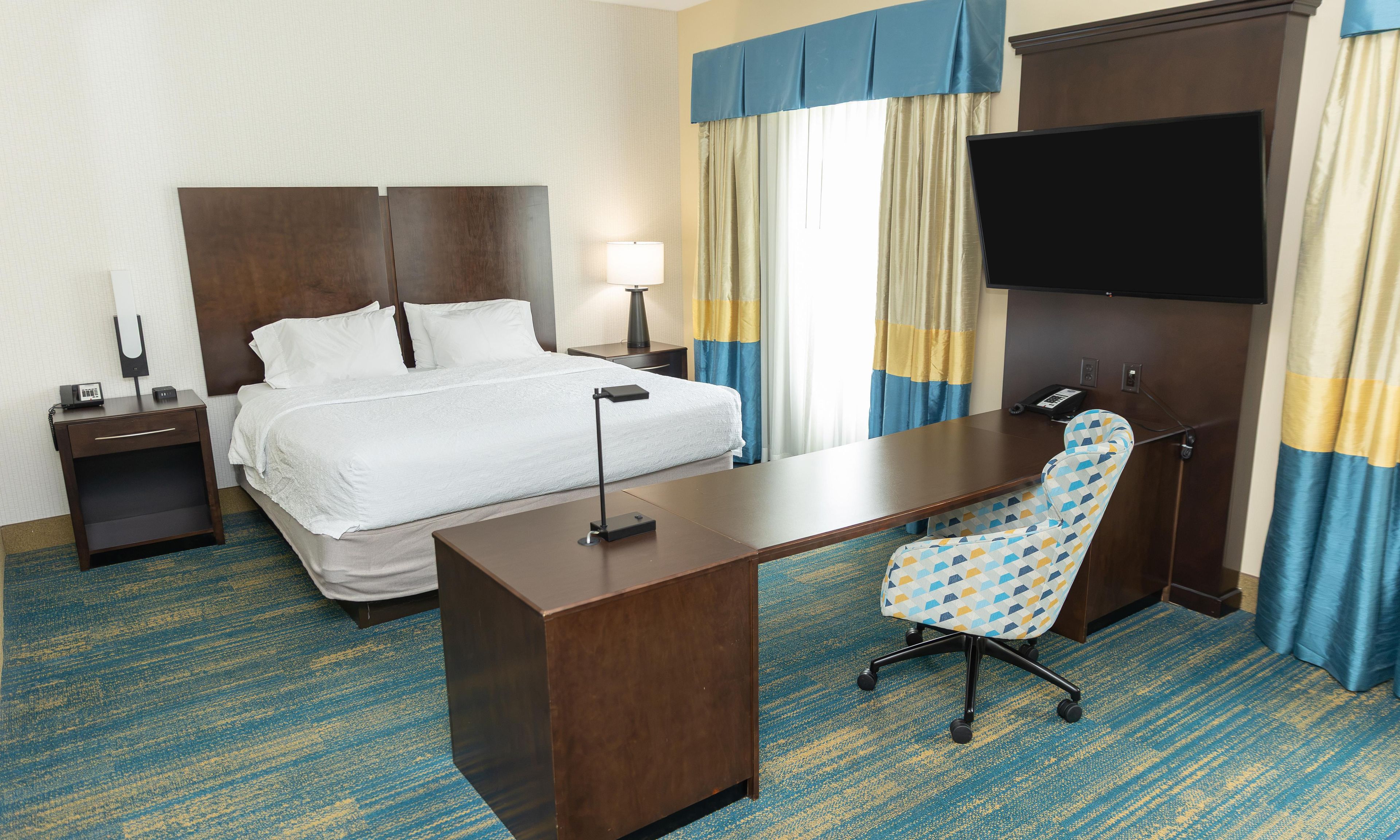 A hotel room with a bed, desk, chair, and a flat-screen TV.