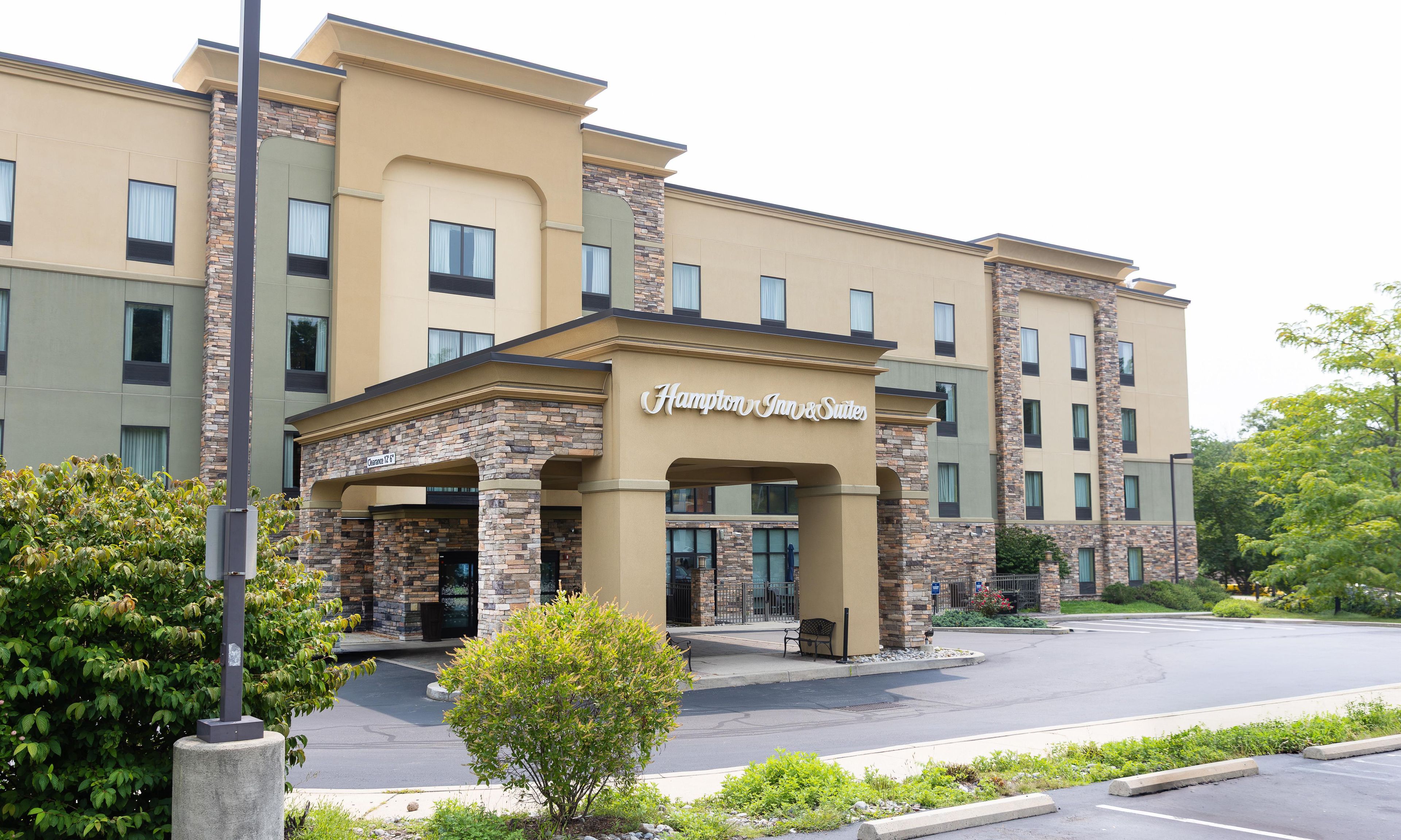 Un hotel Hampton Inn & Suites con fachada de piedra, múltiples ventanas y una entrada despejada.