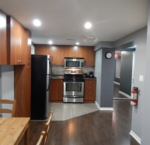 Una cocina moderna con armarios de madera, electrodomésticos de acero inoxidable, una mesa de comedor y un reloj en la pared.