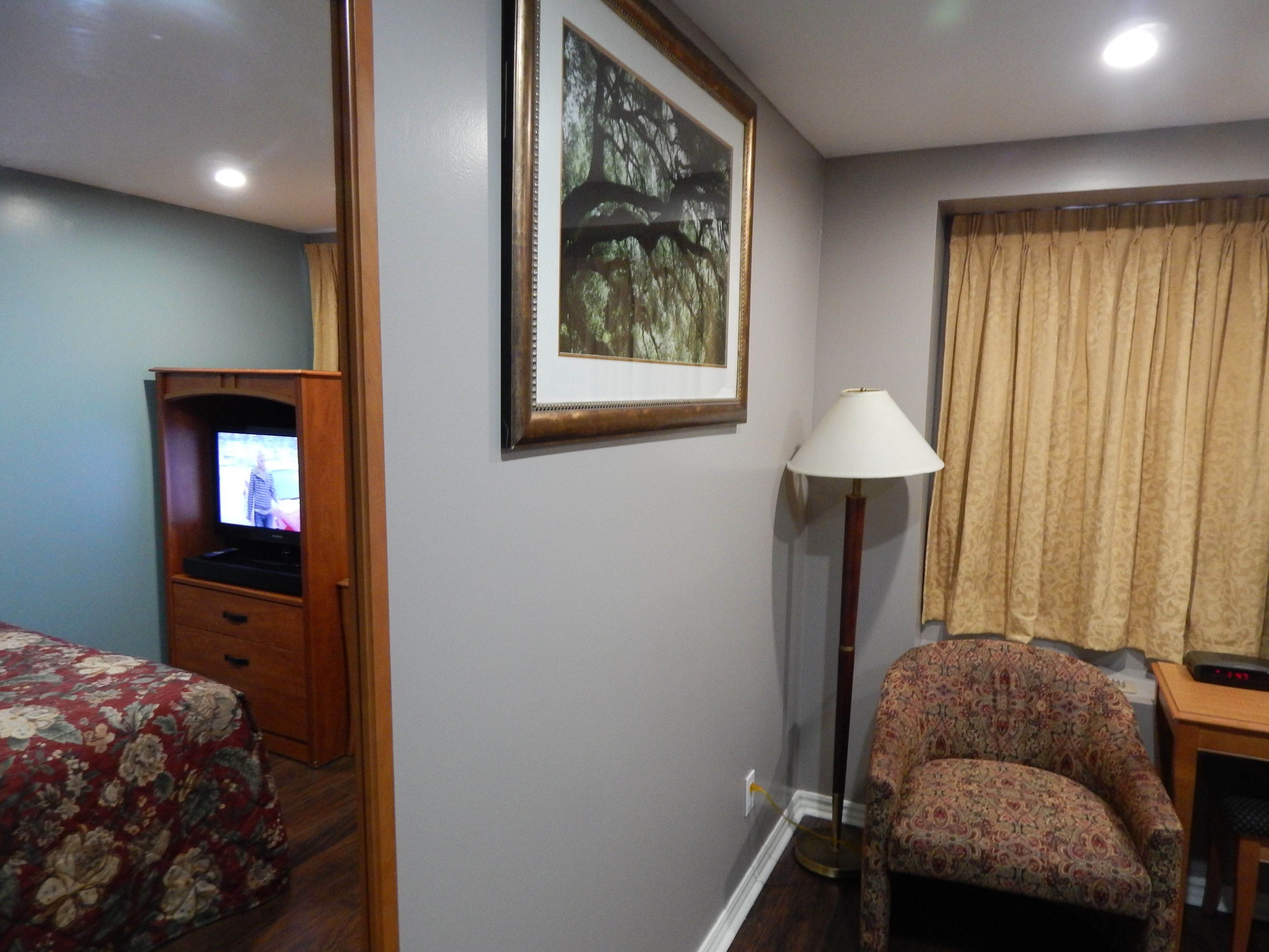 Ein Hotelzimmer mit Bett, Stuhl, Fernseher, Lampe und einem Bild an der Wand.