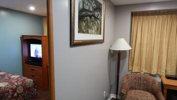 Ein Hotelzimmer mit Bett, Stuhl, Fernseher, Lampe und einem Bild an der Wand.
