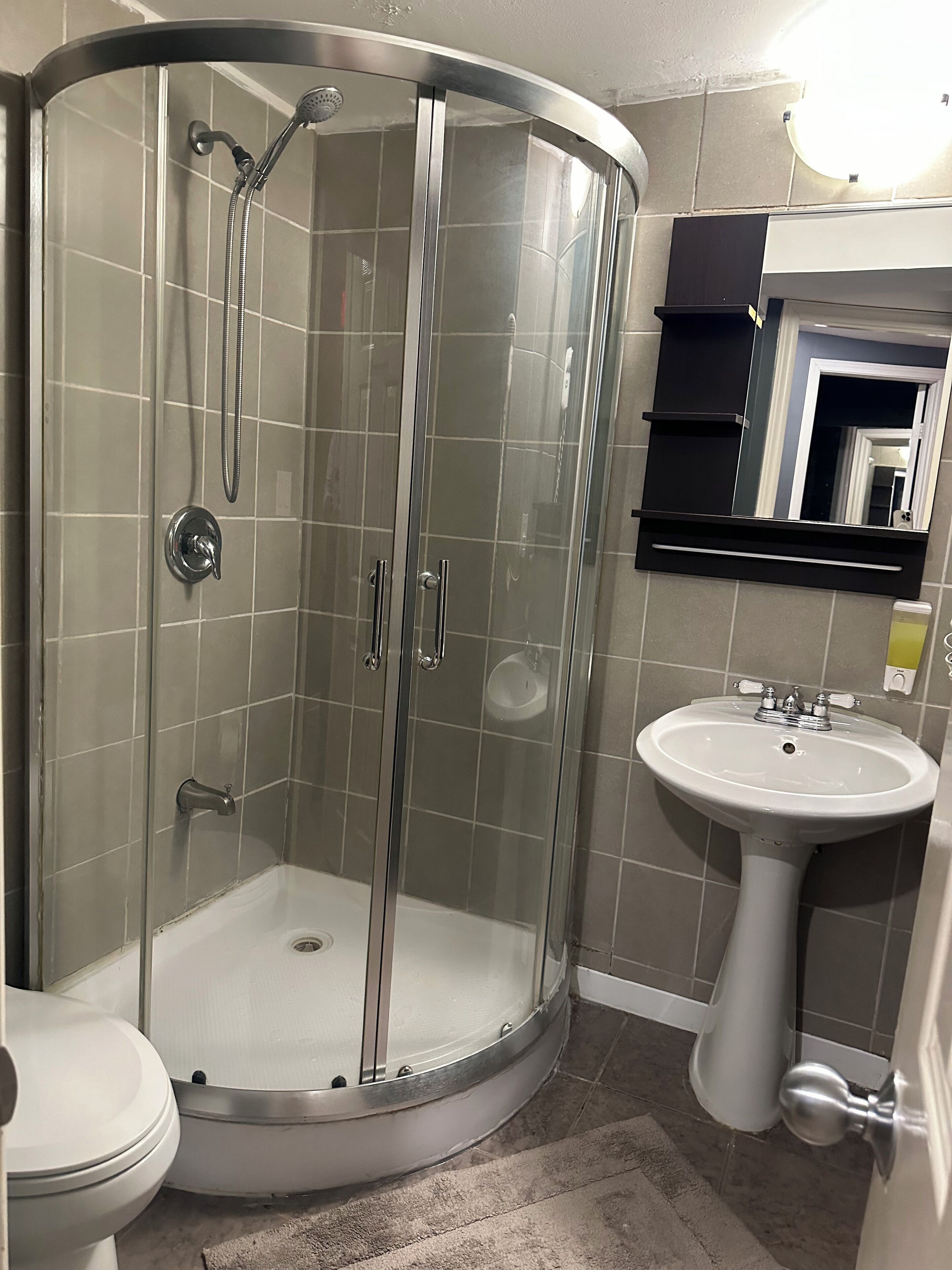 Een moderne badkamer met een douchecabine van glas, een wit zuinig wastafeltje en een toilet.