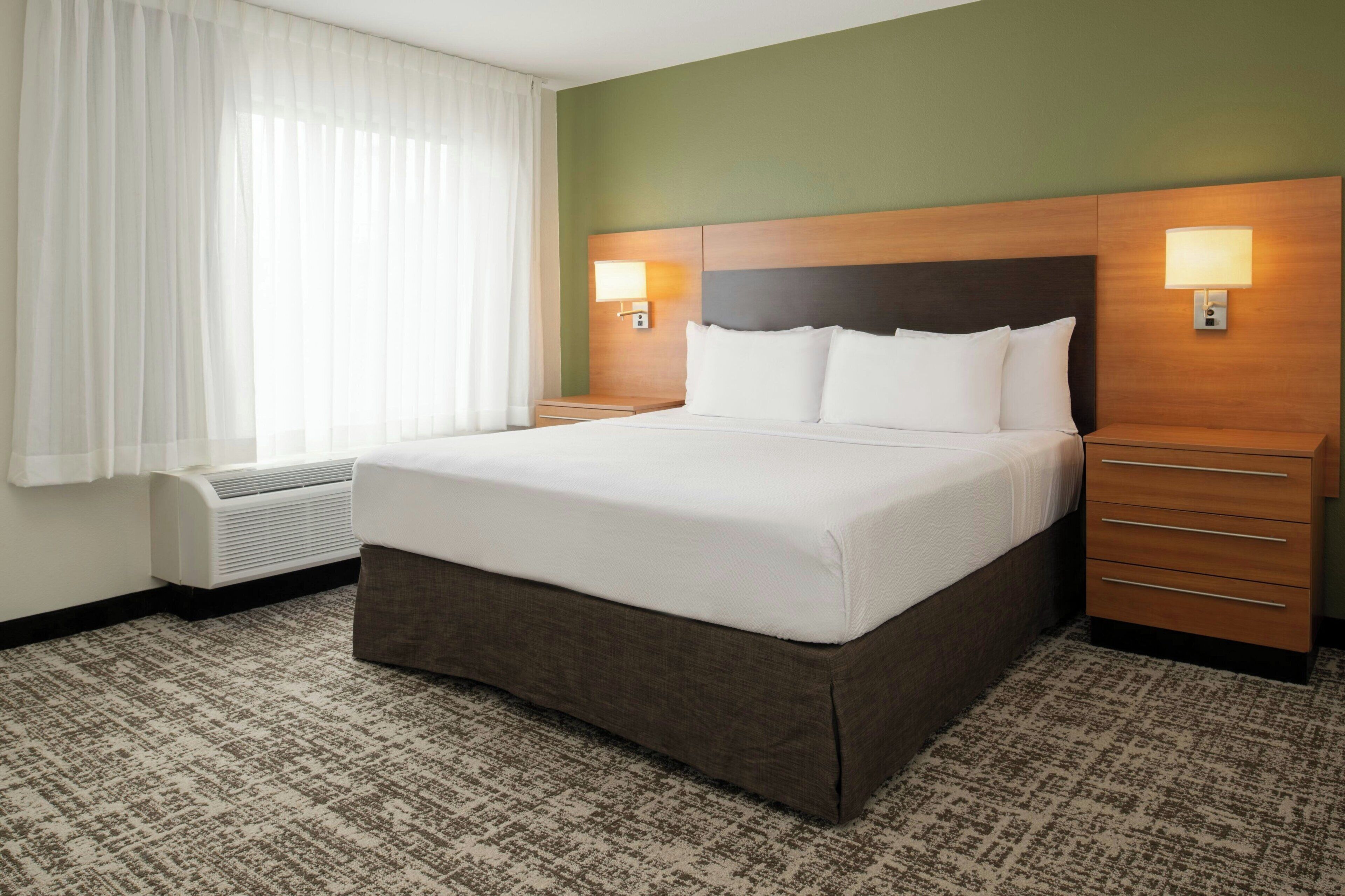A hotel room with a large bed, a bedside table, a lamp, and a window with curtains.
