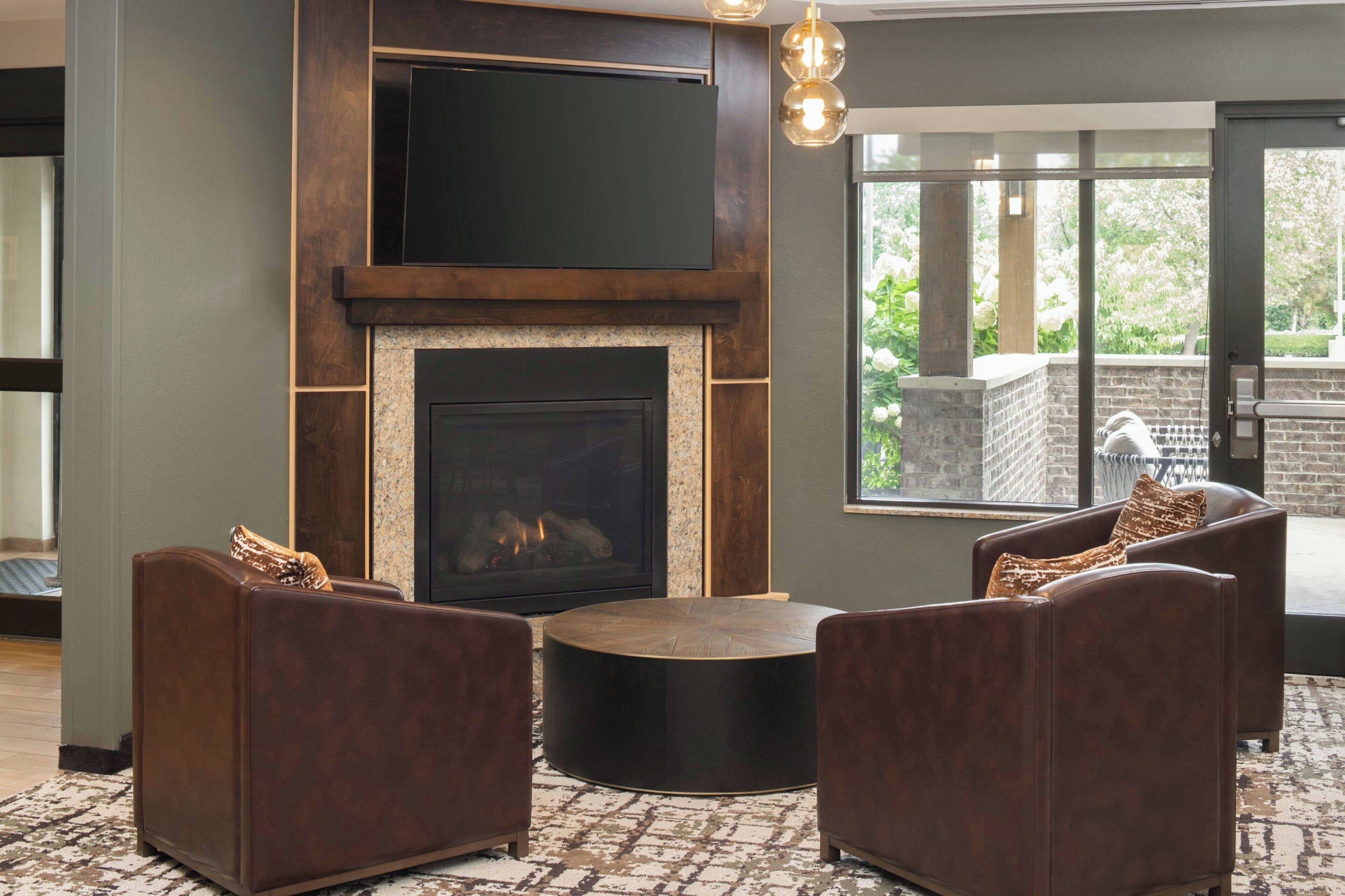 A modern living room with a fireplace, leather sofas, and a large window offering a view of the outdoors.