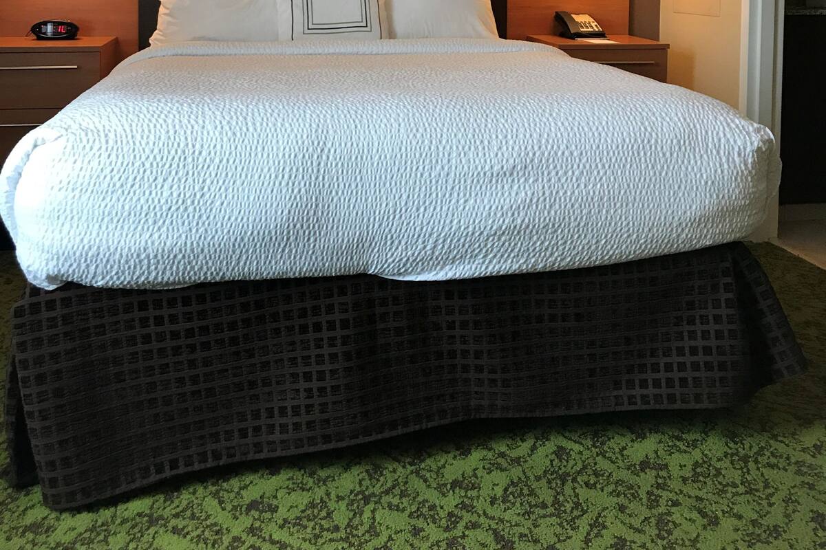 A hotel room with a large bed, two bedside tables, a headboard, and two wall-mounted lamps.