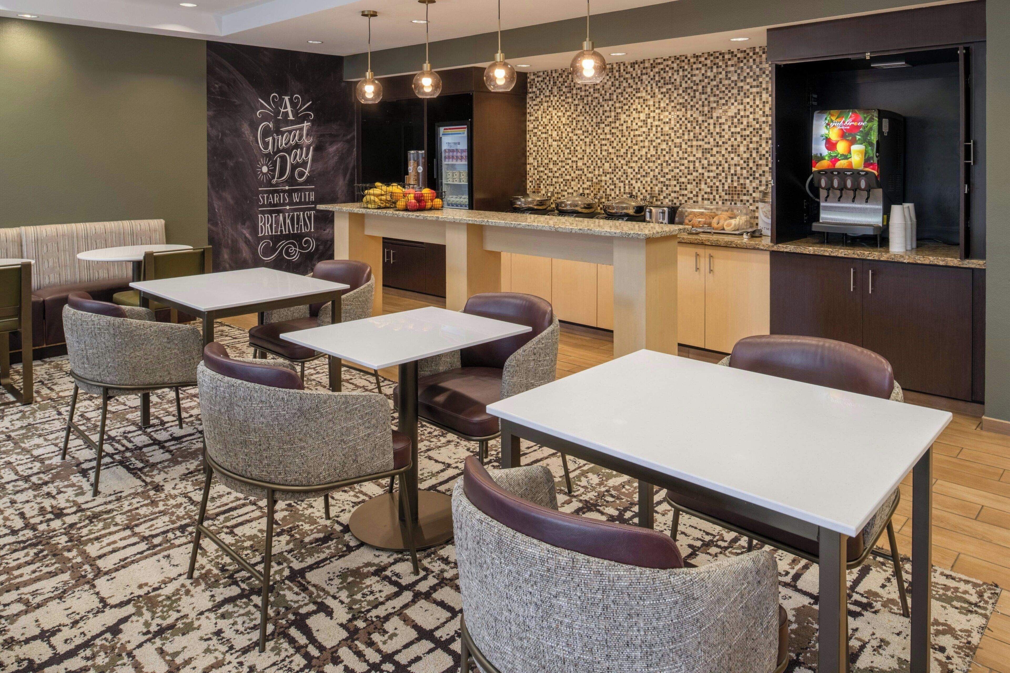 A modern restaurant with a bar area, seating with tables and chairs, and a kitchen visible in the background.