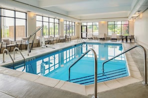 An indoor swimming pool with clear blue water, surrounded by lounge chairs and a sunbed area.