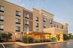 A multi-story hotel with a modern facade, a covered entrance, and a parking area with a 'Welcome' sign.