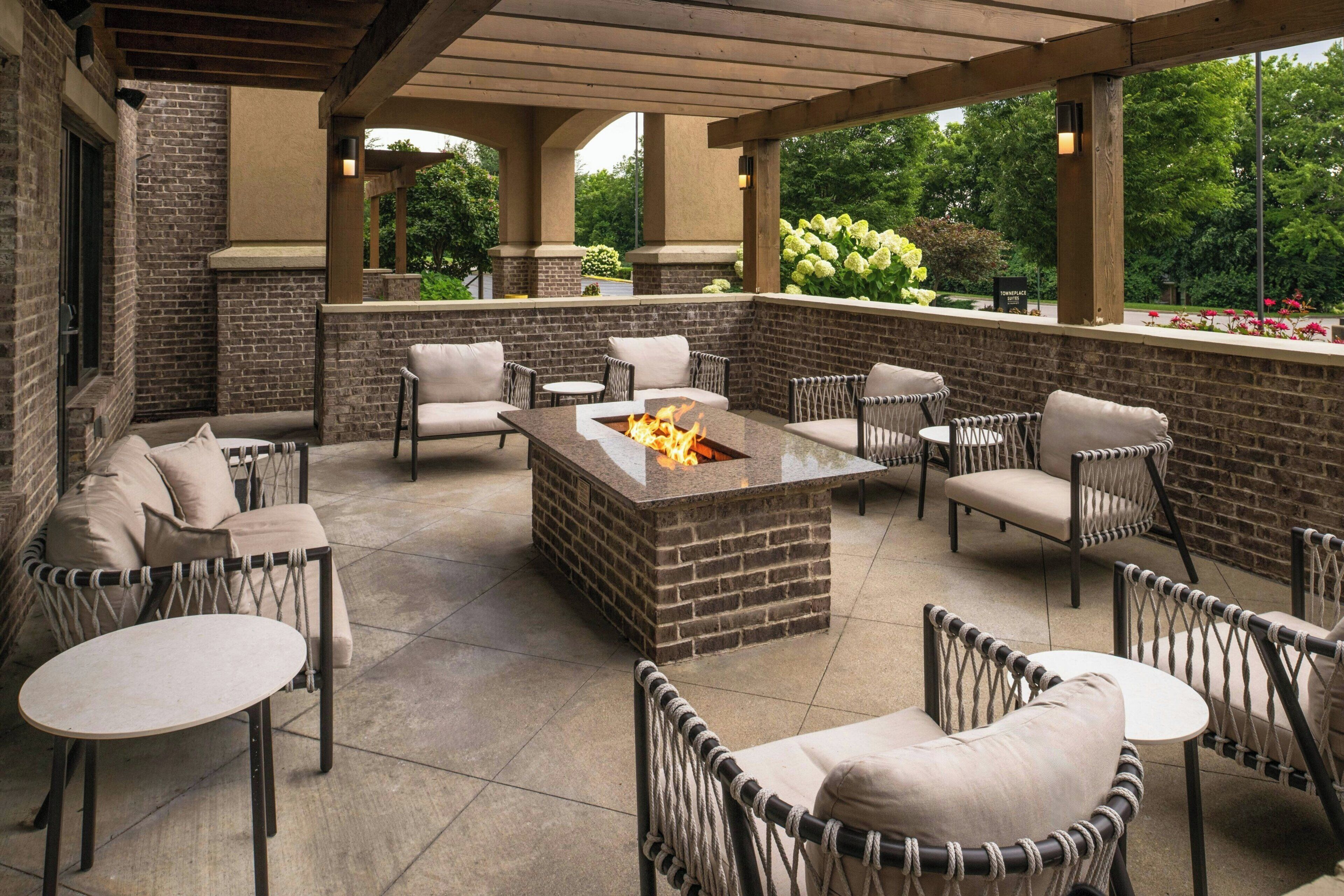 An outdoor patio with brick walls, wicker furniture, and a central fire feature.