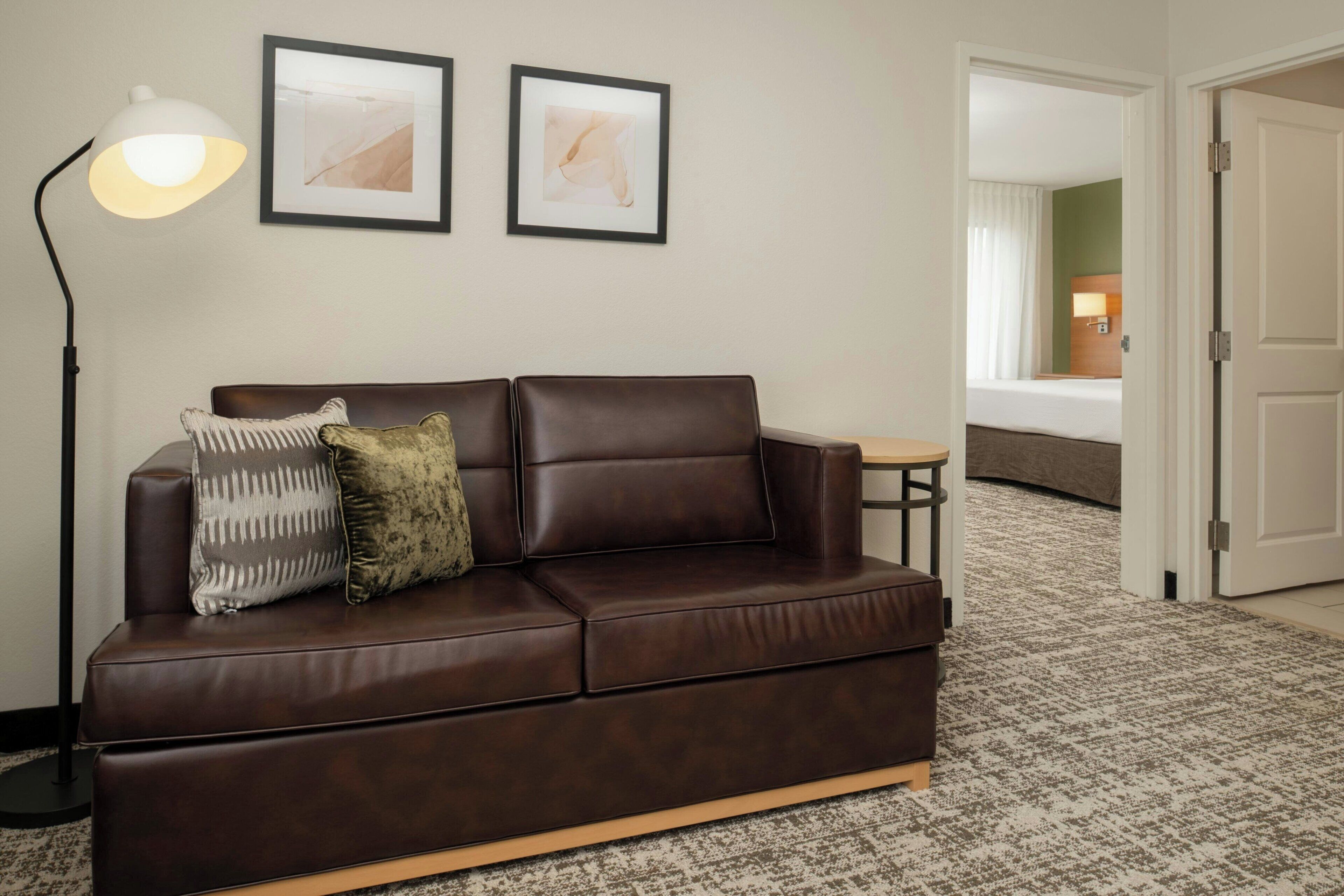 A brown leather sofa with two pillows, a floor lamp, and two framed abstract paintings on the wall.