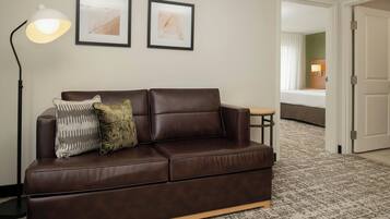 A brown leather sofa with two pillows, a floor lamp, and two framed abstract paintings on the wall.