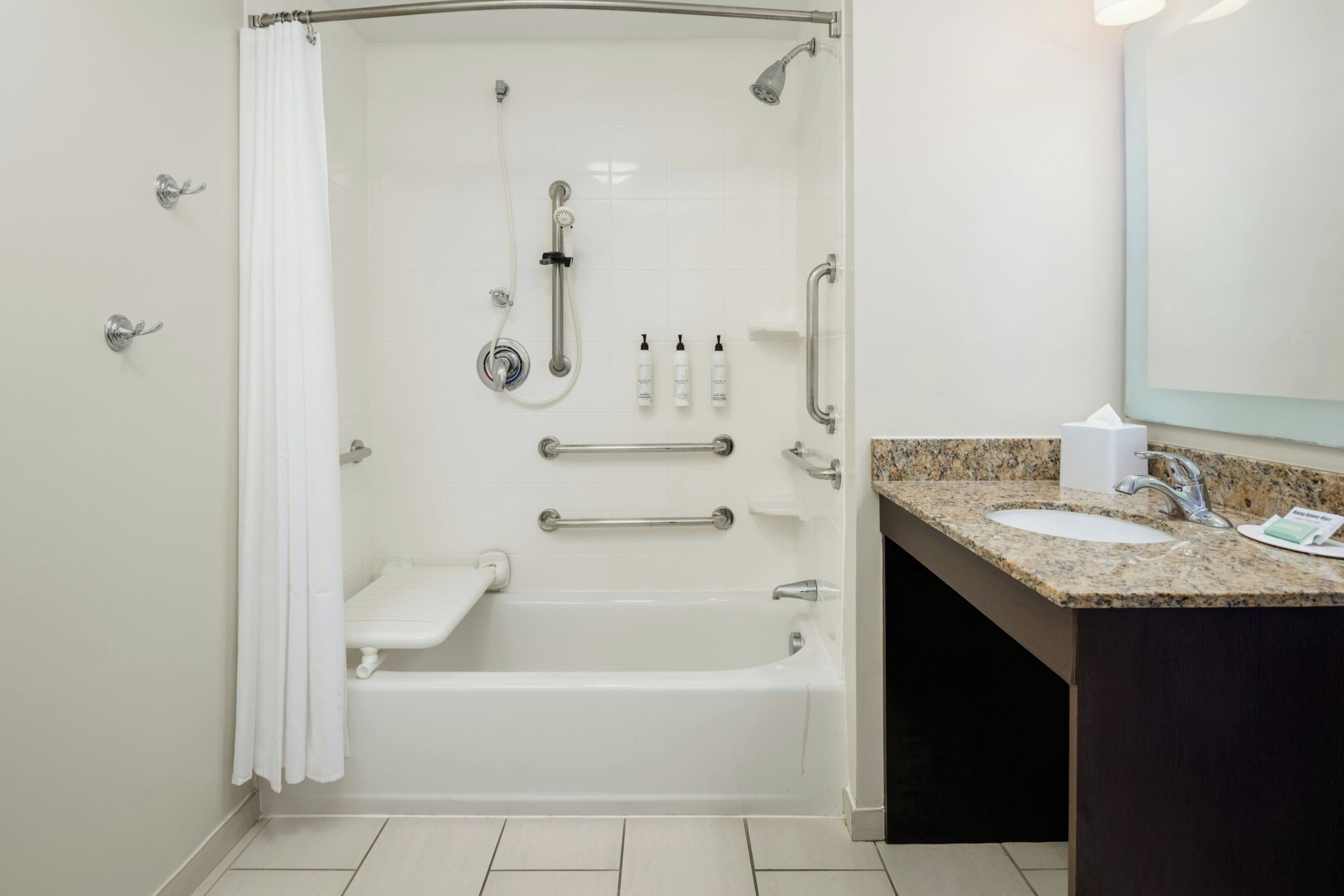 A modern bathroom with a walk-in shower, grab bars, a vanity with a sink, and a mirror.