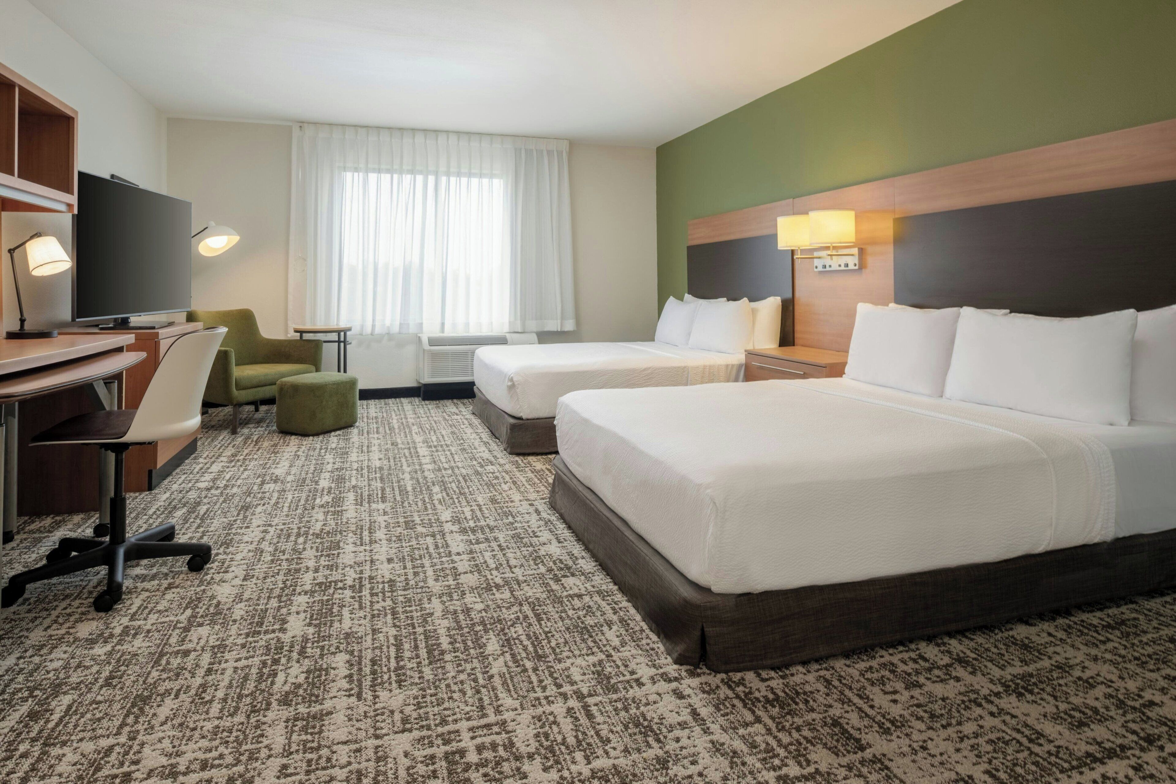 Een hotelkamer met twee bedden, een bureau, een stoel, een televisie en een raam met gordijnen.