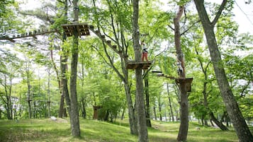 Uma plataforma de cabana na árvore com uma ponte de corda e uma pessoa escalando.