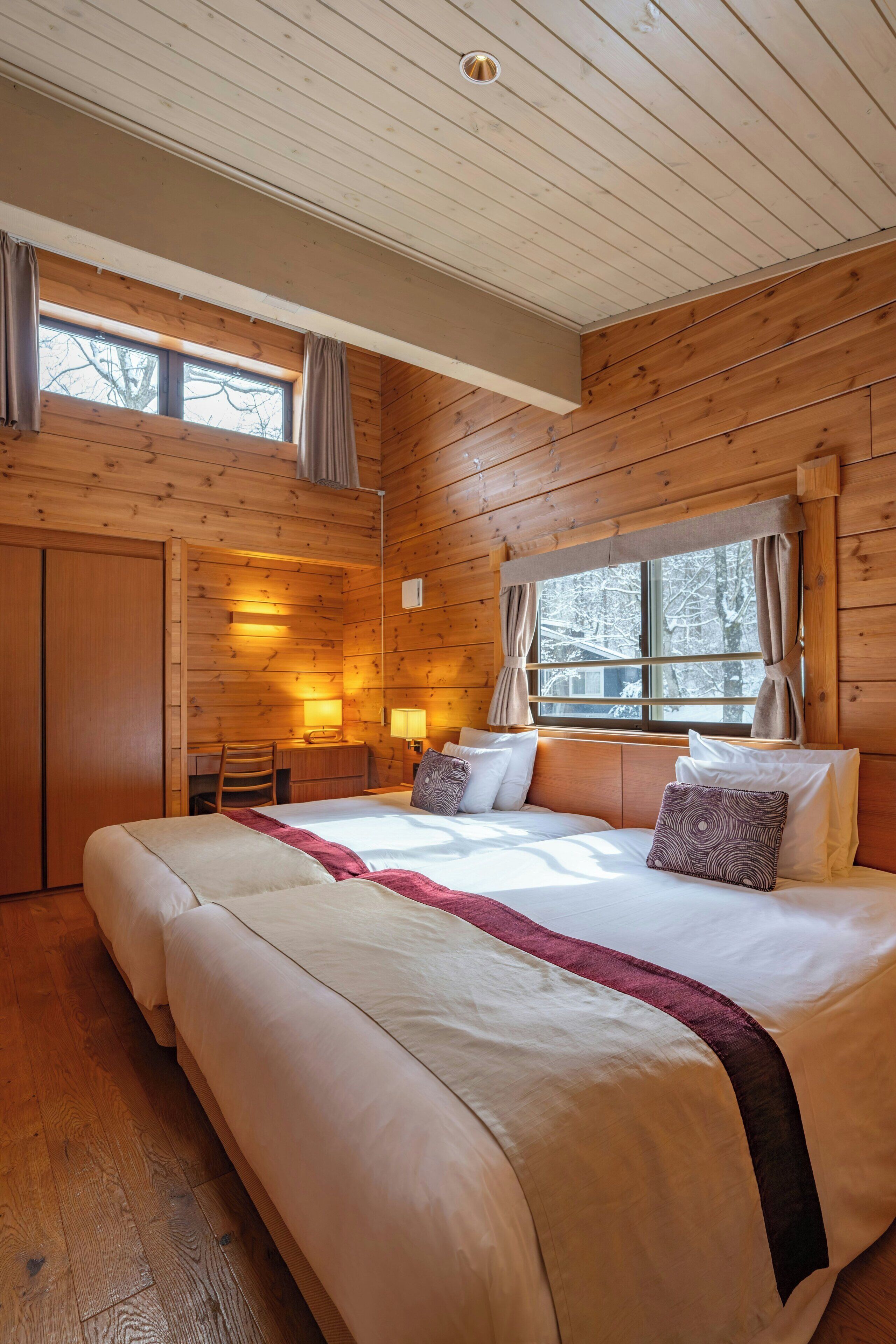 A wooden cabin bedroom with a large bed, a desk, and a window with curtains.