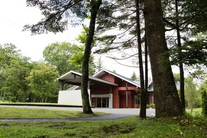 A modern building with a red facade and white roof, surrounded by trees and a grassy area.