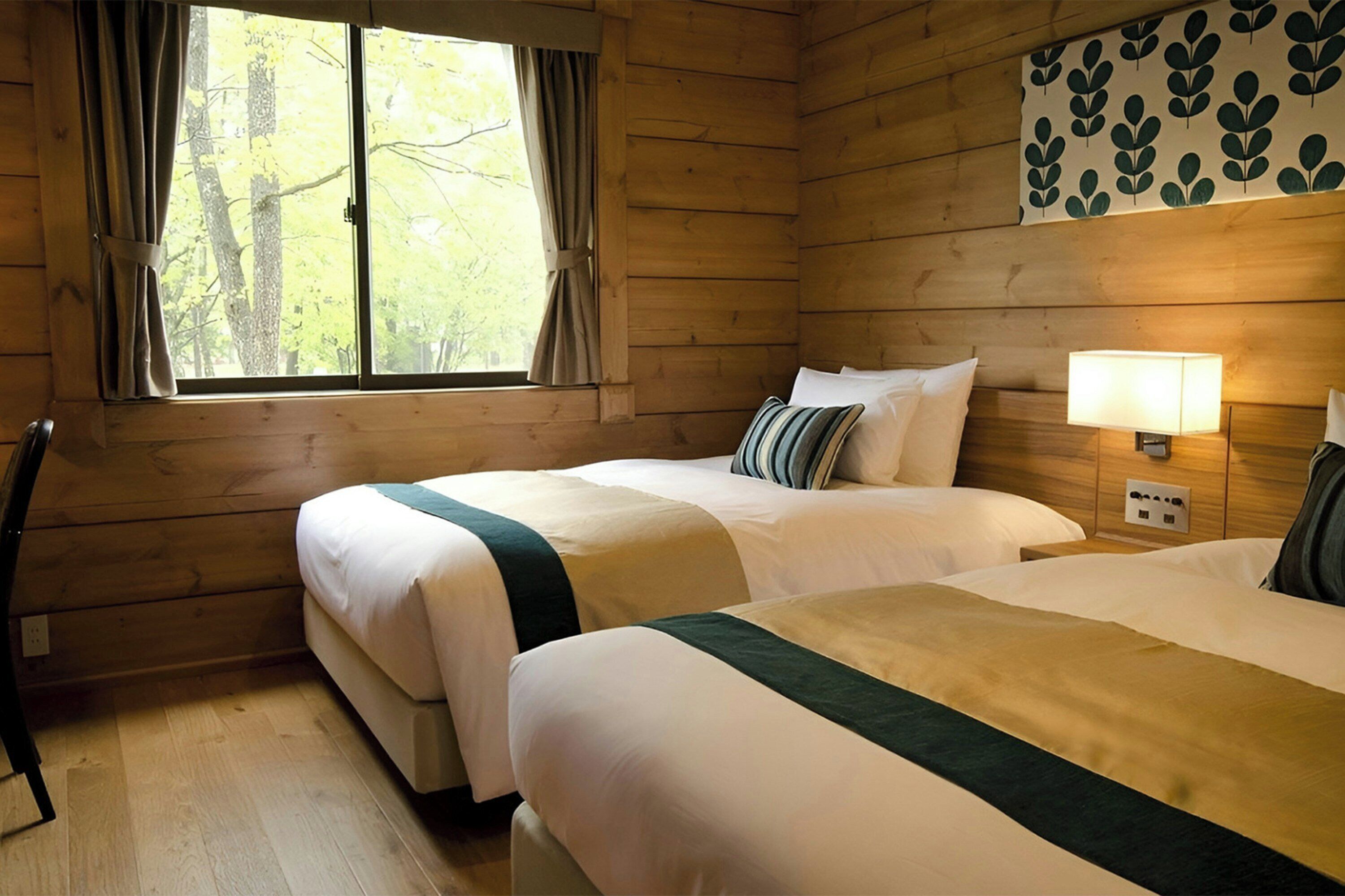 Una habitación de cabaña de madera con dos camas, una ventana con cortinas, una lámpara fijada a la pared y un tapiz decorativo en la pared.