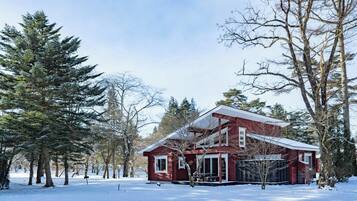 A red cabin with a large window and a balcony, surrounded by snow and trees.