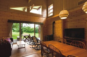 Interior de madera con una mesa de comedor, sillas, un sofá, un televisor y un área de patio con vistas a zonas verdes.