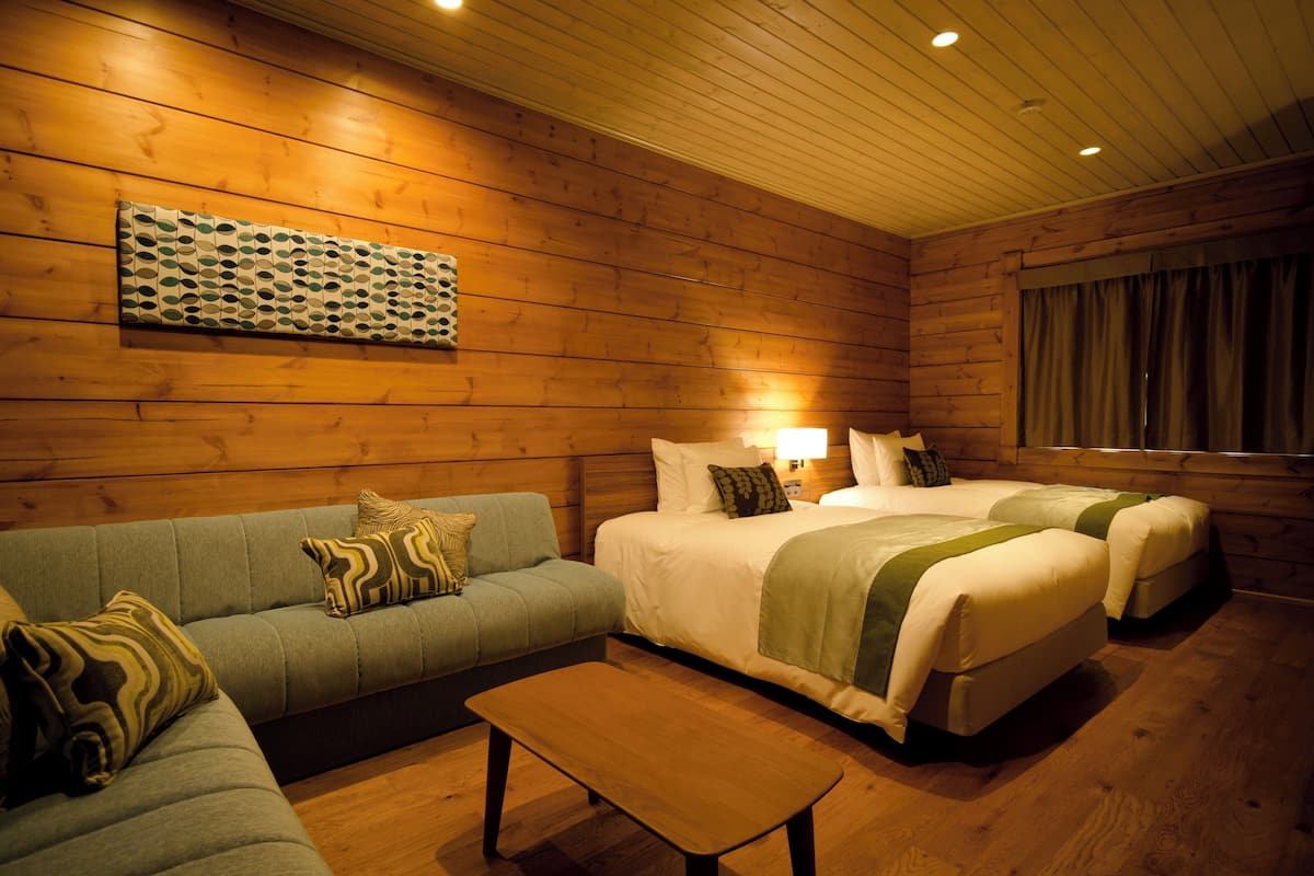 A cozy room with wooden walls, a sofa, two beds, and a small table.
