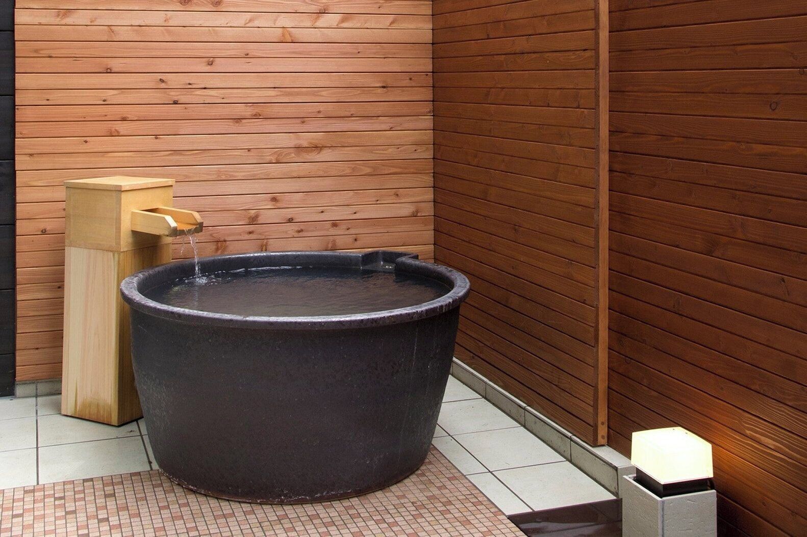A wooden spa area with a large black hot tub, a wooden foot bath, and a tiled floor.